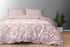 A king size bed sheet set in pink with floral patterns, including two pillow covers, displayed on a bed with a gray wall in the background and a plant beside the bed.